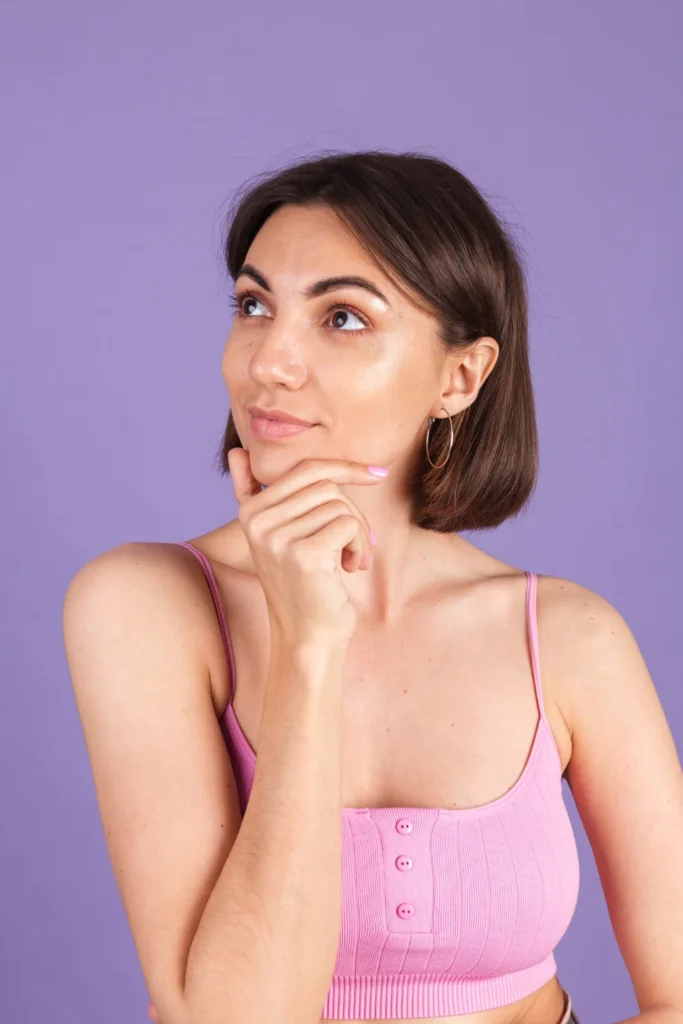 A young woman thoughtfully touching her chin, considering cheek reduction plastic surgery