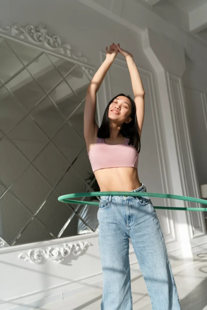 A young woman with long dark hair hula hooping with a green hoop