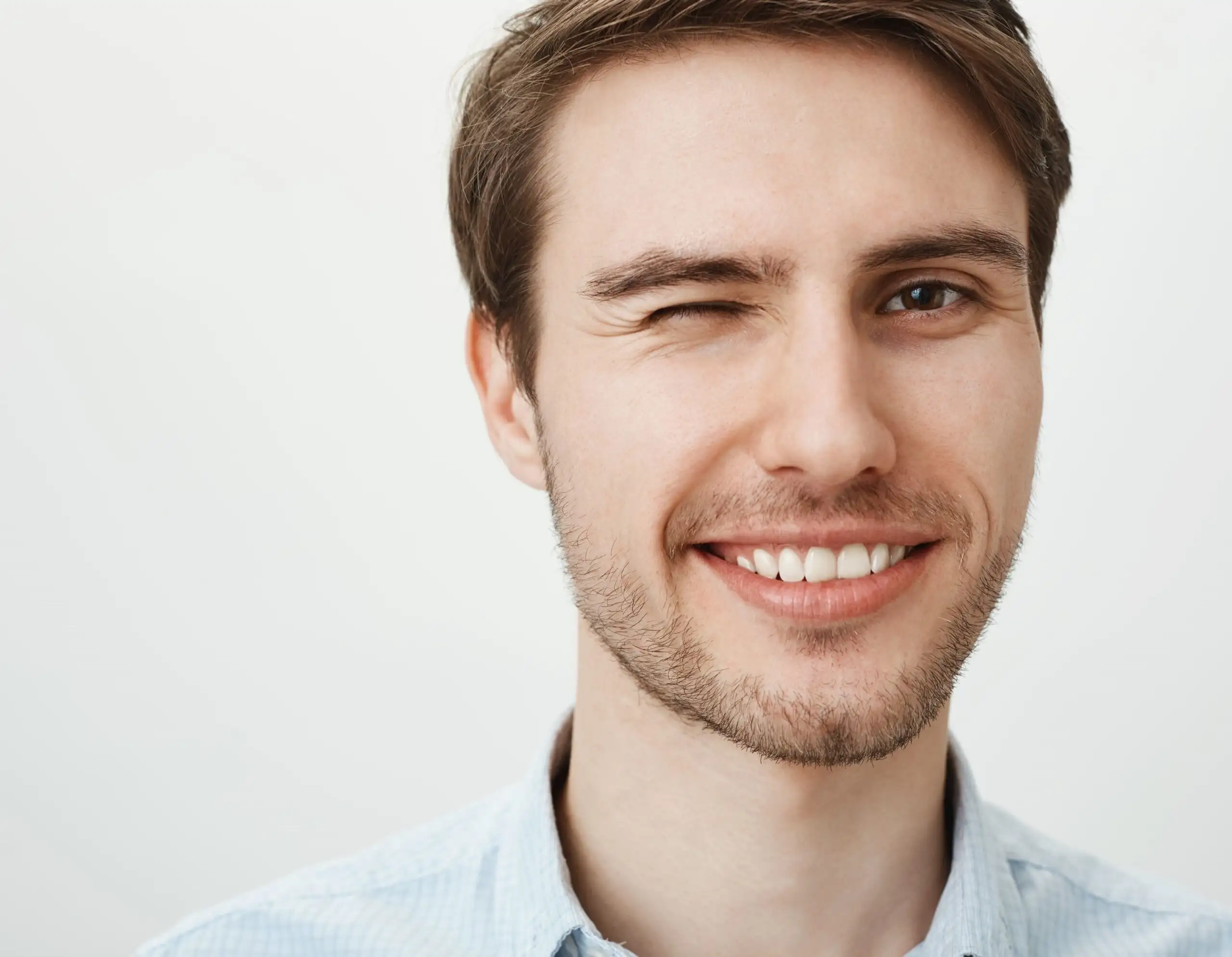 close up handsome young man with white teeth smiling pleased winking cheeky