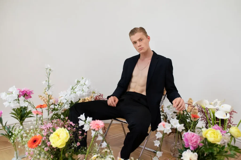 Man wearing an unbuttoned suit showing his abs after lipo recovery and surrounded by flowers