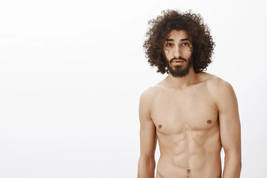 Shirtless man with curly hair flexing abs after abdominoplasty