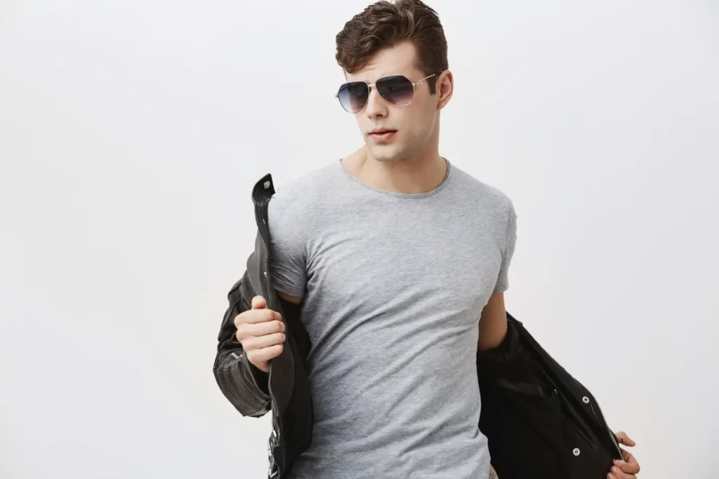 Man wearing sunglasses and removing leather jacket while flexing the results of his FaceTite procedure