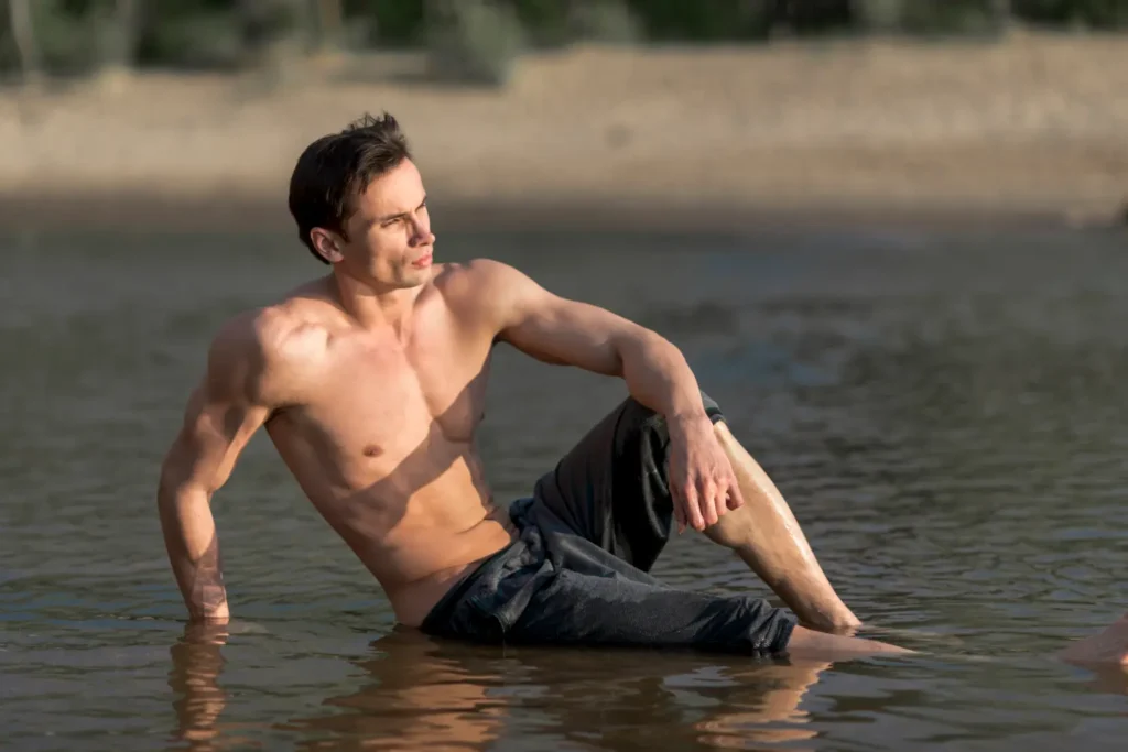 Shirtless man posing by the sea with his sculpted abs after liposuction recovery