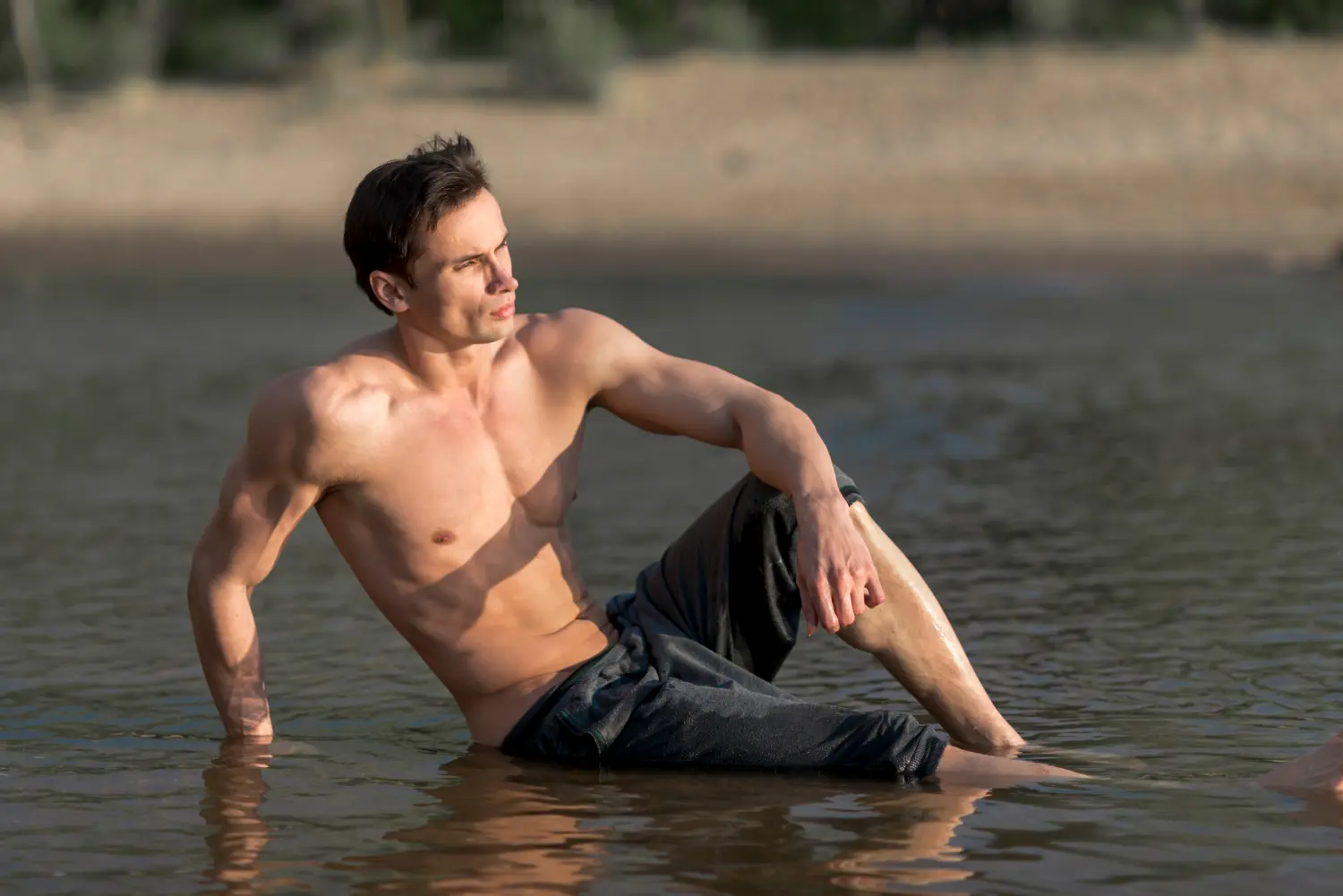 Shirtless man posing by the sea with his sculpted abs after liposuction recovery