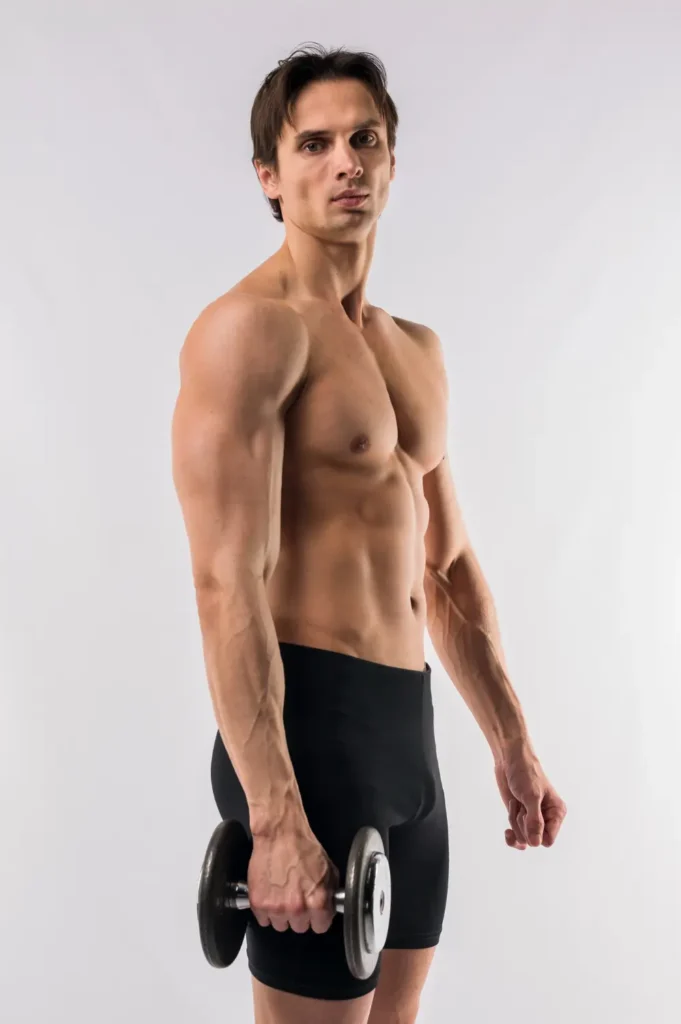 A shirtless, muscular man with short brown hair stands on a light background