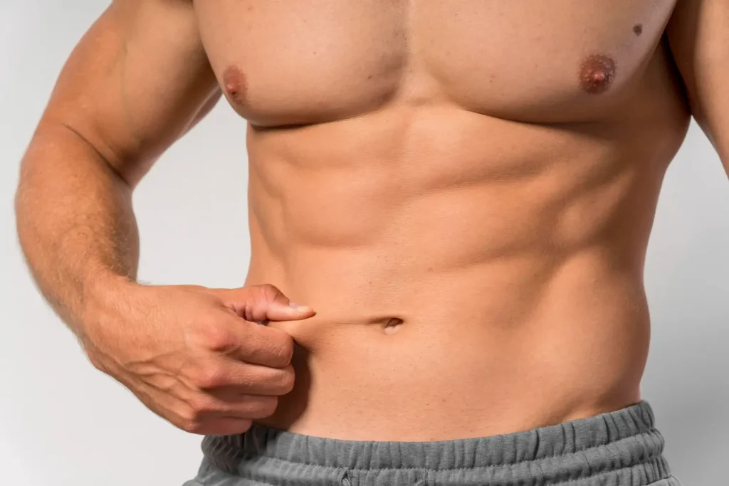 Close-up of a man pinching minimal skin near his belly button, showing a firmer, more contoured abdomen that looks better than before a tummy tuck