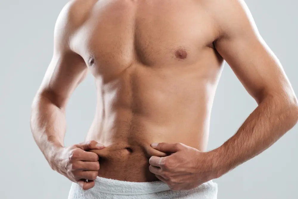 Man pinching the skin around his midsection and belly button area, illustrating concerns about how a tummy tuck can affect the navel's appearance
