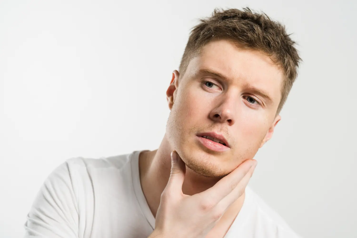 Young man touching his jawline to assess facial contour and the potential benefits of jawline filler