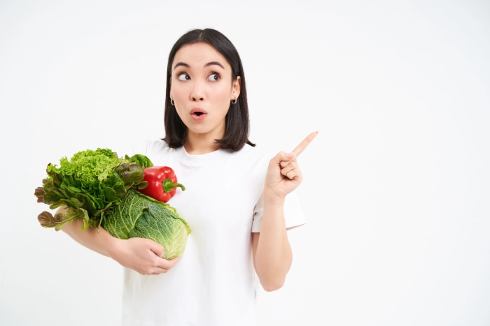 portrait girl with surprised face pointing advertisement holding green vegetables concept