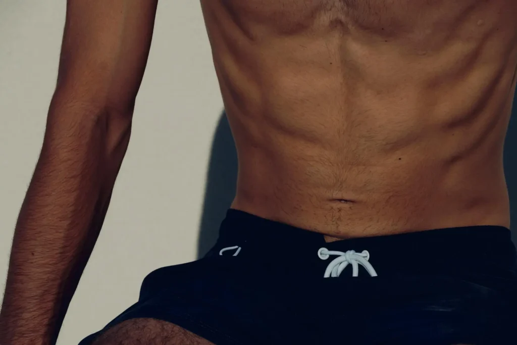 Man wearing board shorts while also flexing his sculpted abdomen after HD lipo