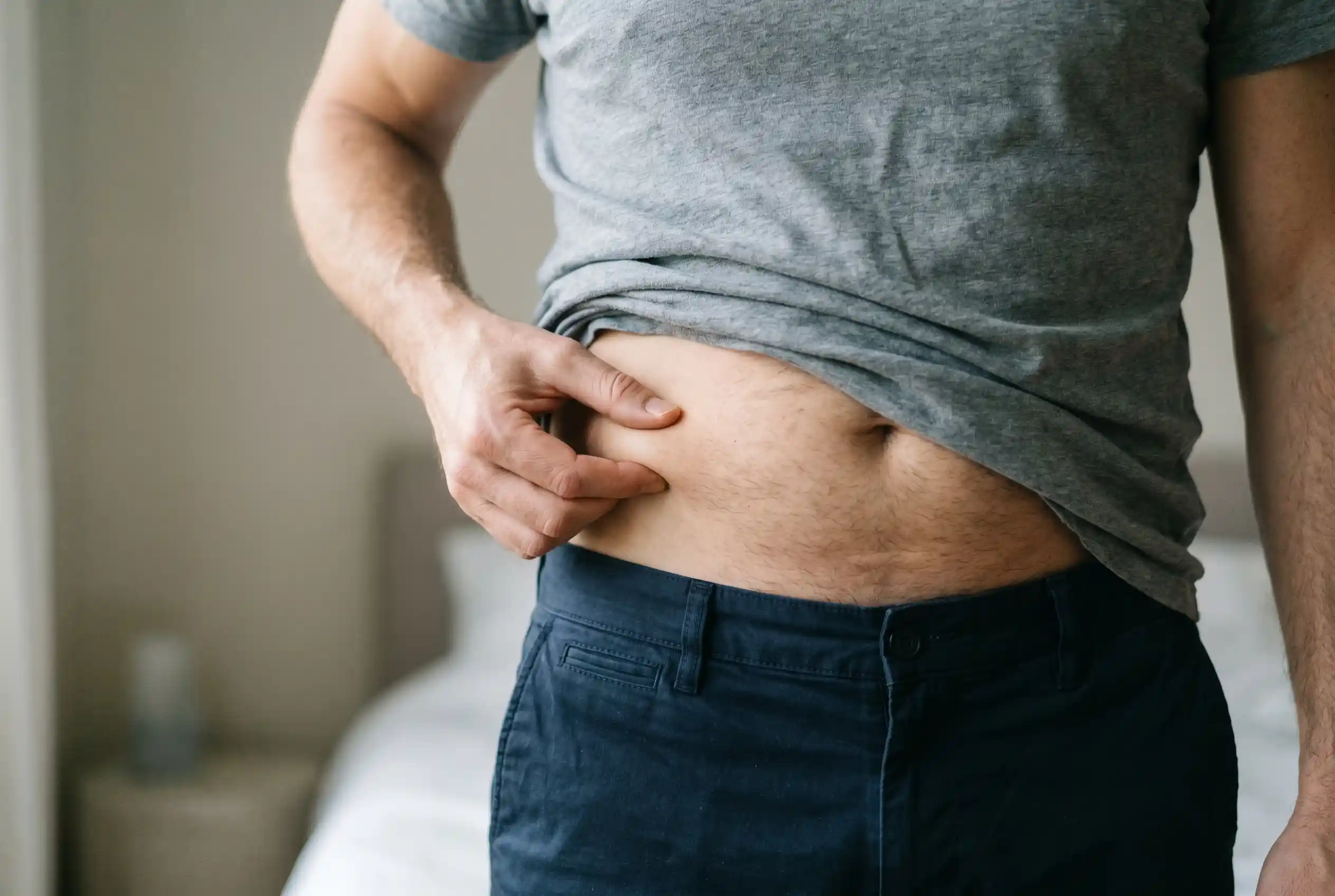 Man pinching belly fat while researching whether tesamorelin burns belly fat