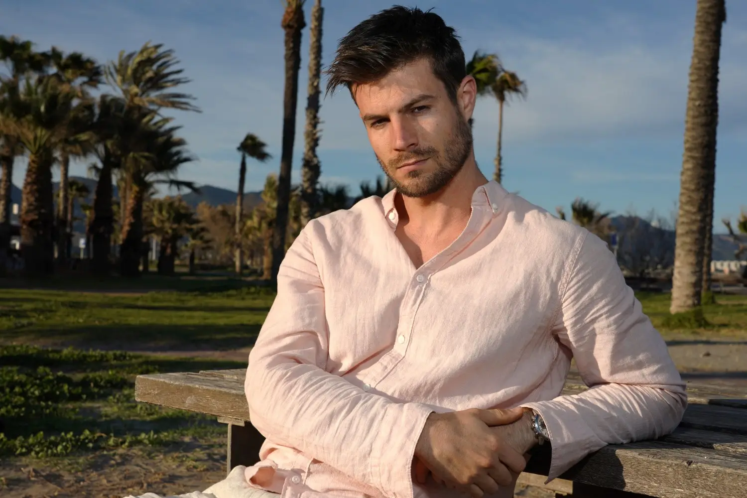 Young hispanic male wearing a pink shirt and posing on the beach