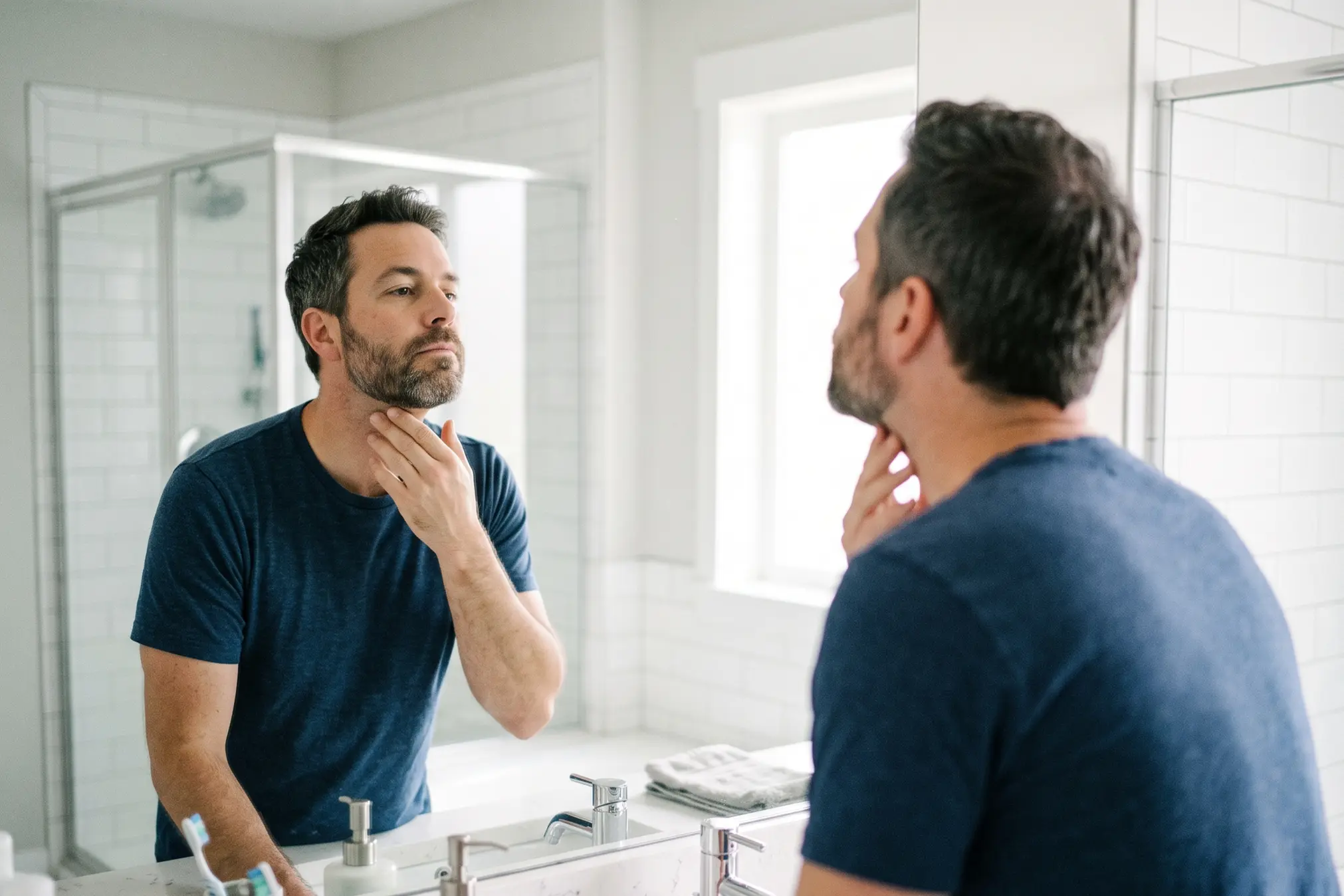 Man examining his jawline in a mirror while researching whether FaceTite will damage his face