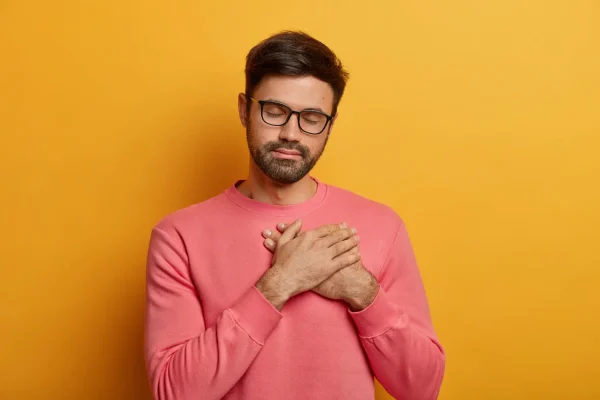 Man wearing pink sweater with orange background and putting both palms on his chest before lipo