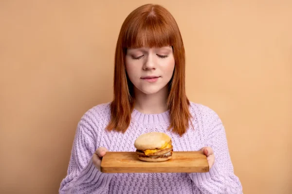 Woman holding a burger but looking sad because she needs to avoid it after PRP hair treatment