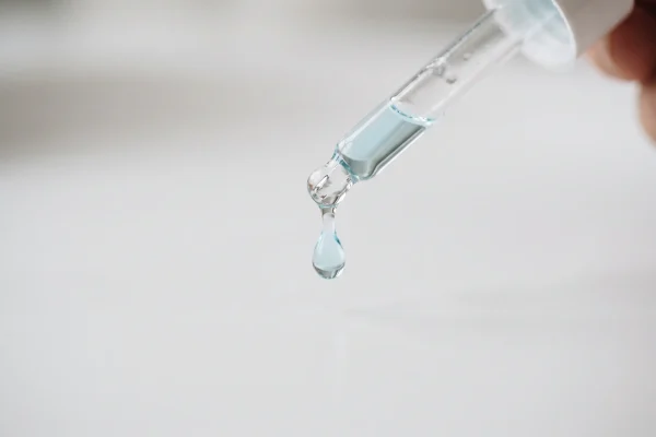 Blue-tinted copper peptide serum drop from a glass dropper