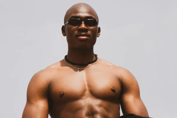 Shirtless man wearing shades and flexing his sculpted chest after HD liposuction recovery