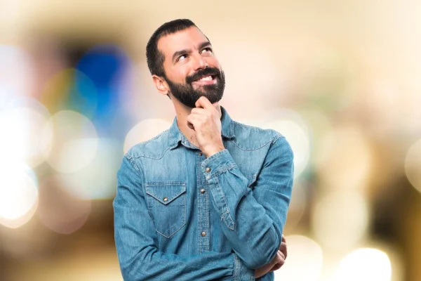 Man wearing blue buttoned shirt thinking if plastic surgery is worth it