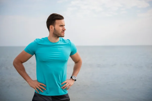 Man wearing blue shirt and flexing manly physique by the sea after thymosin alpha 1 and thymosin beta 4 therapy