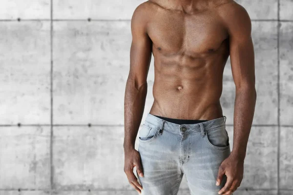 Medium shot of a shirtless man wearing jeans and sporting his sculpted abs after tummy tuck