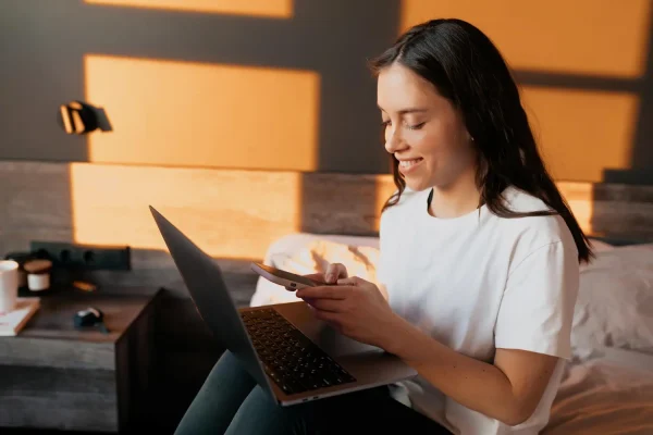 Woman holding phone and laptop trying to book a jawline filler appointment