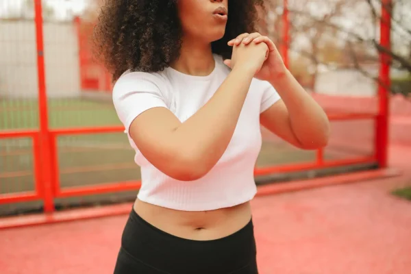 Woman wearing a white top and black leggings exercising outside after tummy tuck recovery