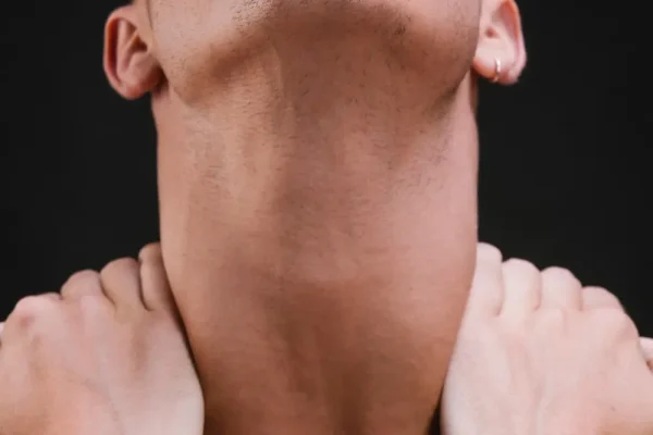 A close-up of a man's neck and jawline being tilted back and manually lifted