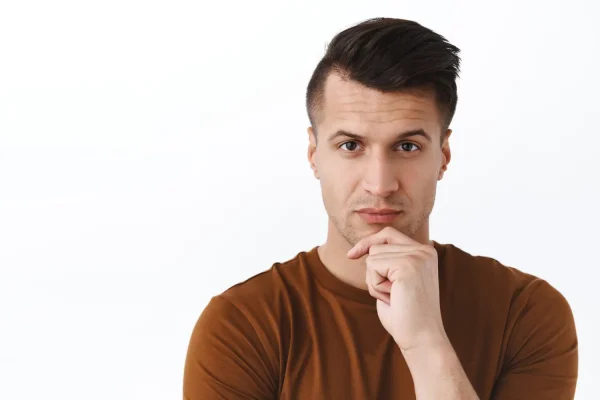A close-up portrait of a man looking thoughtfully at the camera with his hand to his chin