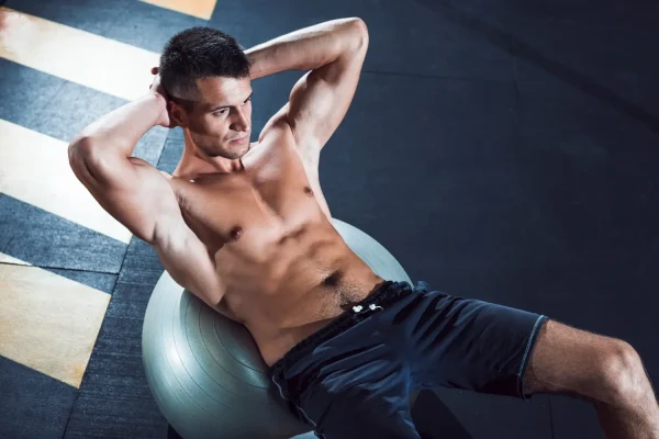 A fit man with prominent abdominal muscles performing sit-ups on a stability ball