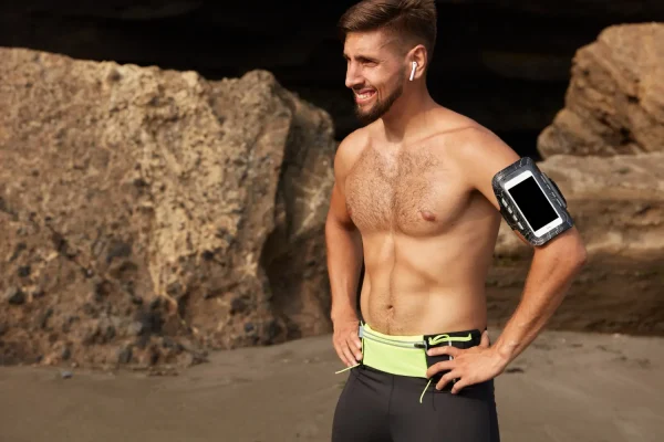 A fit, muscular man smiling on the beach, illustrating the sculpted physical appearance often desired by individuals