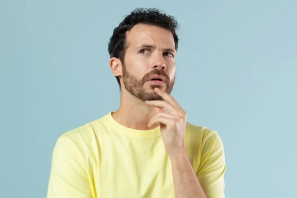 A man in a yellow t-shirt with a curious and focused expression