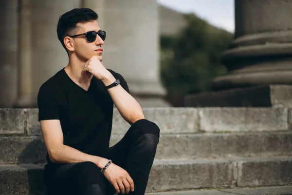 A man in sunglasses sits on stone steps in a pensive pose, reflecting the curiosity surrounding whether Botox is considered plastic surgery