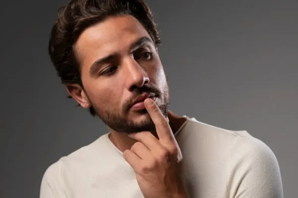 A man with a contemplative look on his face, touching his finger to his mouth