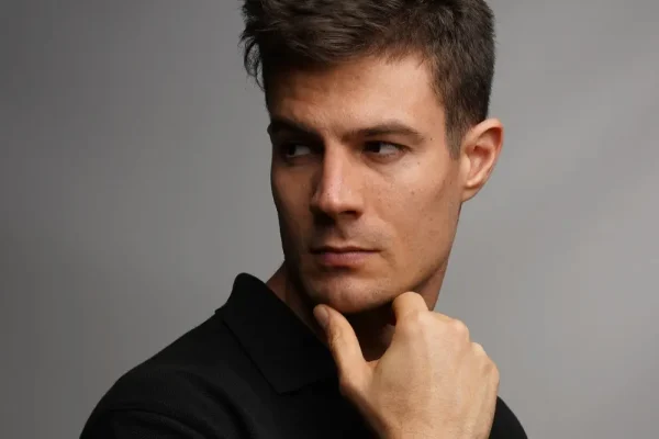 A man with a sharp profile gazes to the side with a hand on his chin