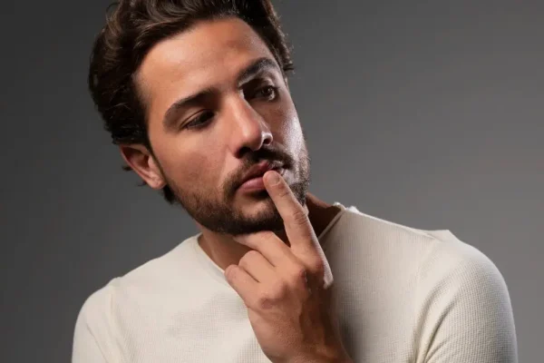 A man with a thoughtful expression is touching a firm area on his jawline, visually demonstrating how fibrosis after a cosmetic treatment