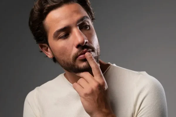 A medium shot of a contemplative man with dark hair and a beard, resting his chin on his hand as if considering his progress