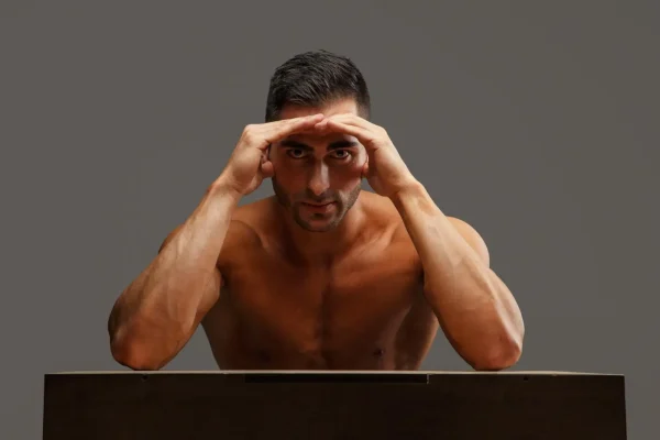 A muscular man with a concerned expression rests his head on his hands, illustrating the frustration and aesthetic worry