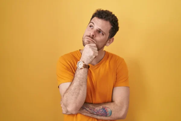 A pensive man with a beard and curly hair looks upward, resting his chin on his hand with a skeptical