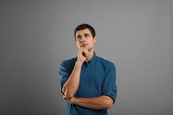 A portrait of a pensive young man in a blue plaid shirt holding his chin and looking upwards