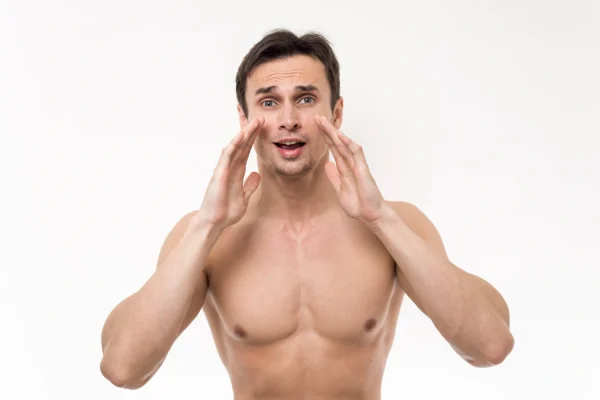 A shirtless man with both hands framing his face and neck with a surprised