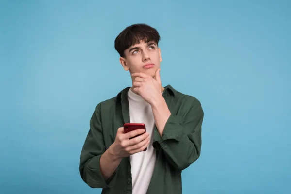 A thoughtful young man holding a phone and looking up as if in contemplation