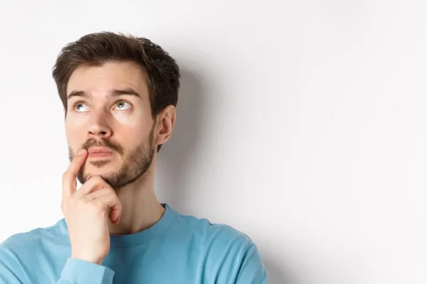 A thoughtful young man looking upward with a hand on his chin, symbolizing the curiosity and discovery of what Sermorelin
