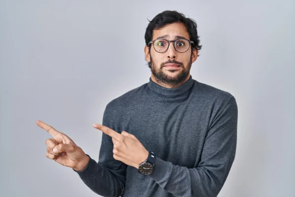A wide-eyed man with glasses pointing in two directions with a surprised expression