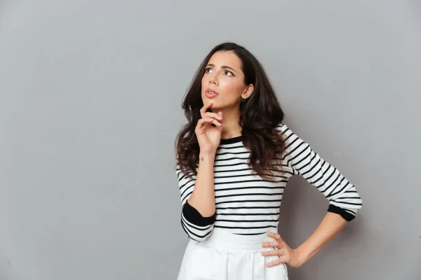 A woman in a striped shirt with a thoughtful expression, hand on chin, looking upward as if contemplating how tirzepatide works in the body