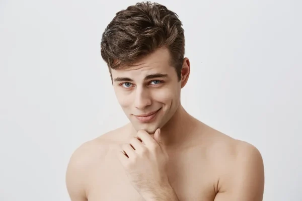 A young man touching his smooth, firm jawline with a smirk, highlighting the skin-tightening