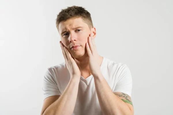 A young man with a concerned expression holding both sides of his face