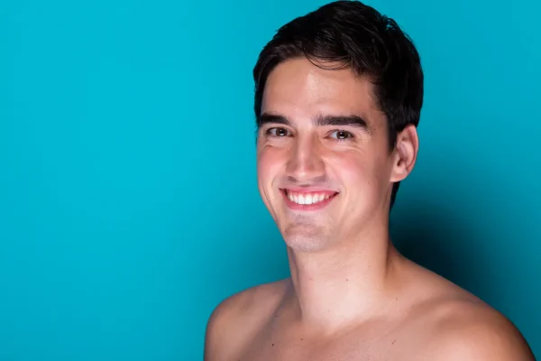 A young man with a defined jawline and smooth skin smiling against a teal background
