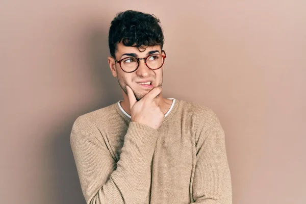 A young man with glasses looks off to the side with a skeptical and uncertain expression