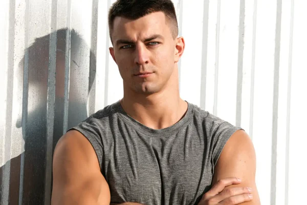 An athletic man with a sharp, sculpted jawline leaning against a wall
