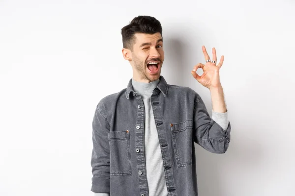 Confident young man winking and showing an ok sign after achieving a younger look